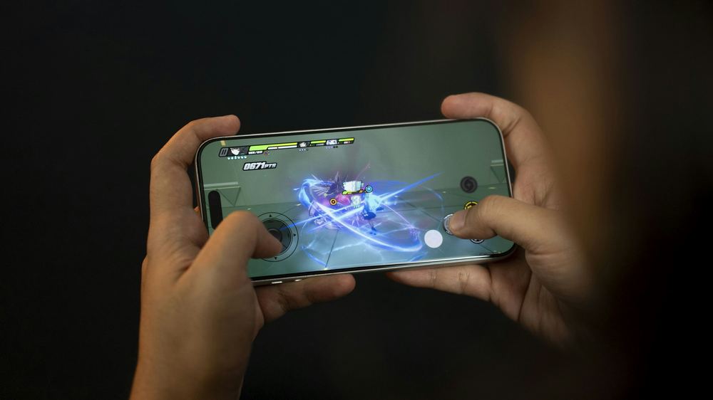 Tangan memegang ponsel untuk bermain gim, melambangkan pengalaman mobile yang nyaman