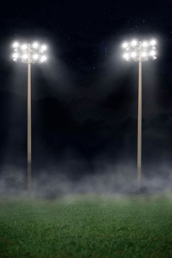 Menara lampu stadion menyala terang di atas lapangan hijau berkabut
